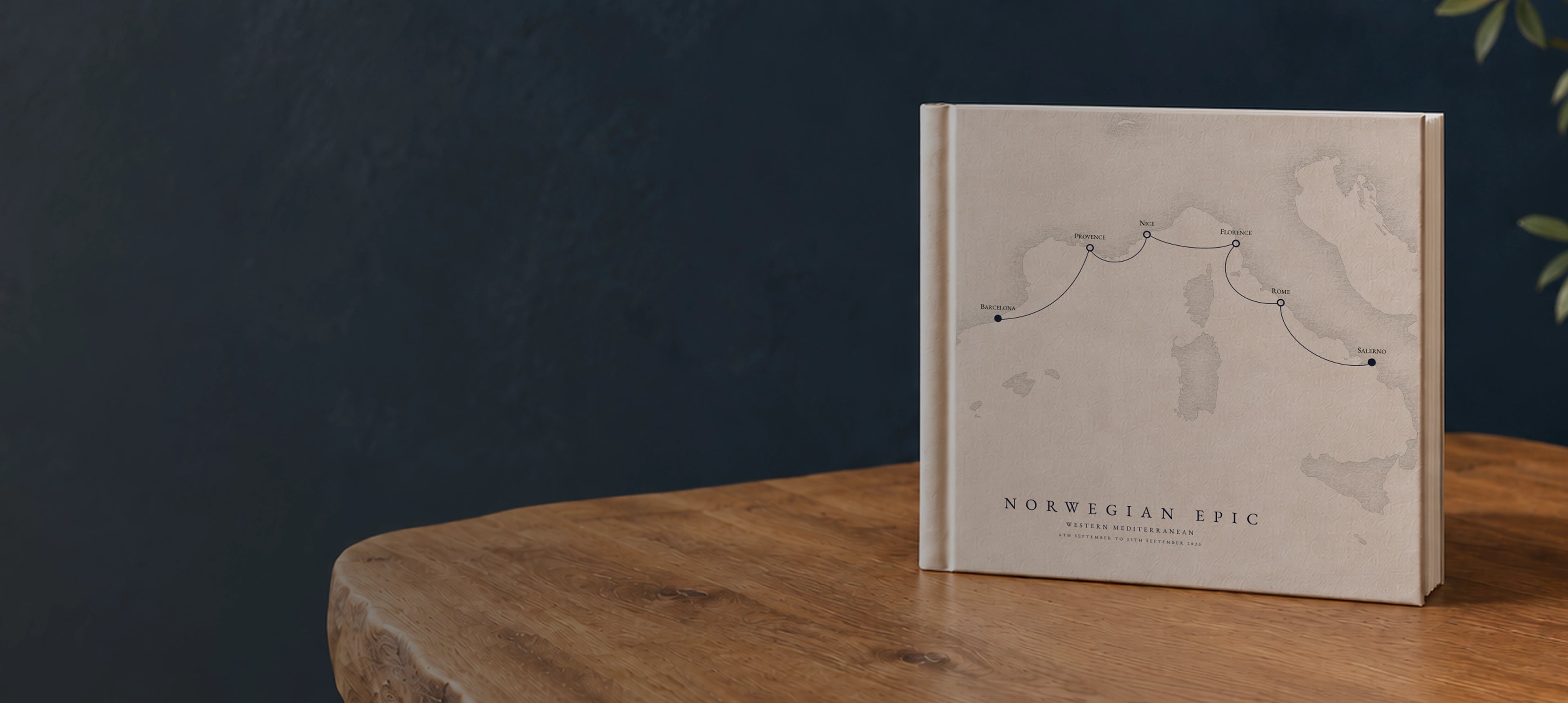 A personalised Portside oatmeal cruise album standing on an oak table, with bespoke itinerary artwork on the cover